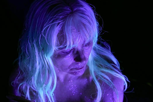 A person with glowing blue hair and skin in darkness