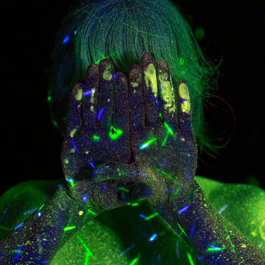 A person with hands covered in glowing green and blue fluorescent paint