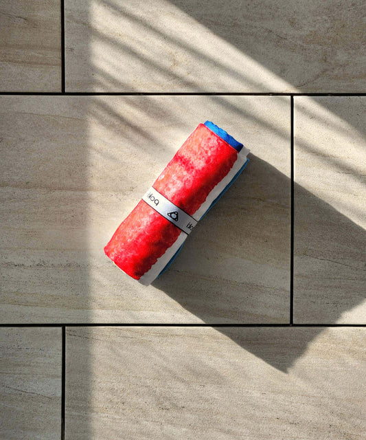 彩虹條紋快乾多用途毛巾卷在石材地面上，陰影投射出精緻的紋理和顏色。