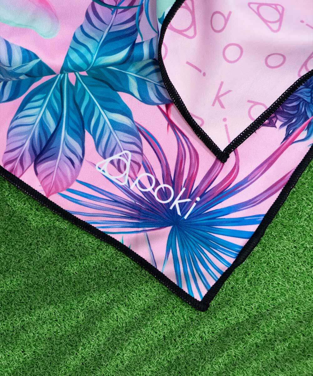 Vivid pink and blue patterned sports towel by POKI, showcasing tropical leaves and logo, perfect for outdoor activities.