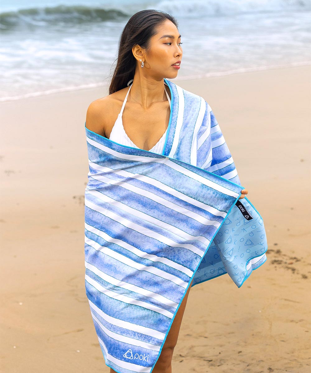 女性在沙灘上穿著水彩條紋快乾毛巾，展示其輕便與時尚設計。